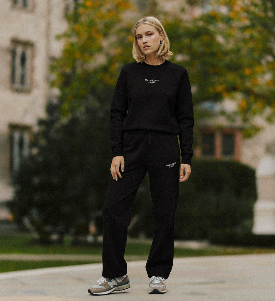 Person wearing a black sweatshirt and pants with text, standing outdoors.