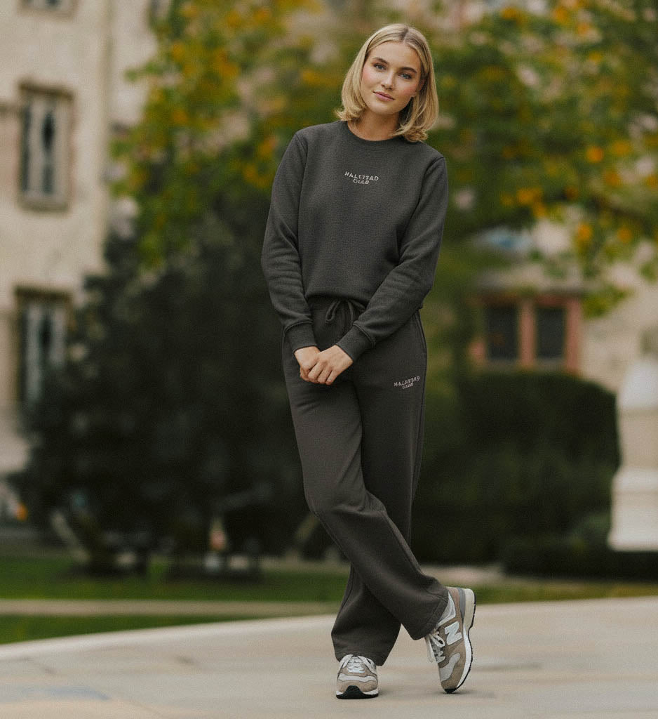 Woman in dark gray sweatshirt and pants walking outdoors with blurred background