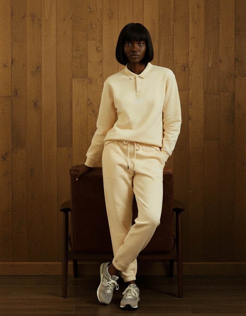 Person wearing a cream-colored hoodie and pants sitting on a wooden chair against a wooden wall.
