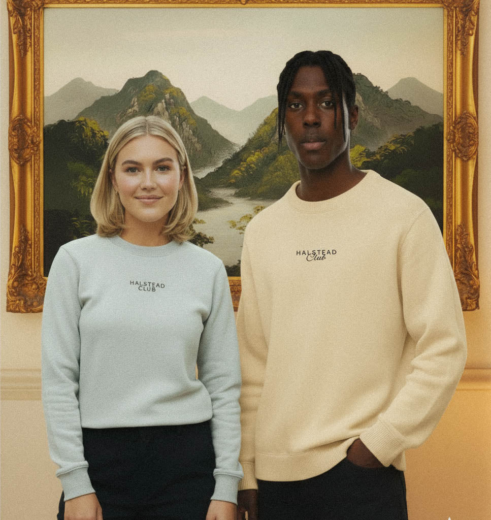 Two people wearing Halstead Club sweatshirts in front of a scenic painting.