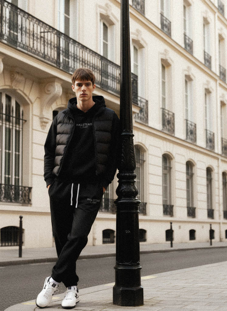 Man in black outfit leaning against a street lamp in an urban setting