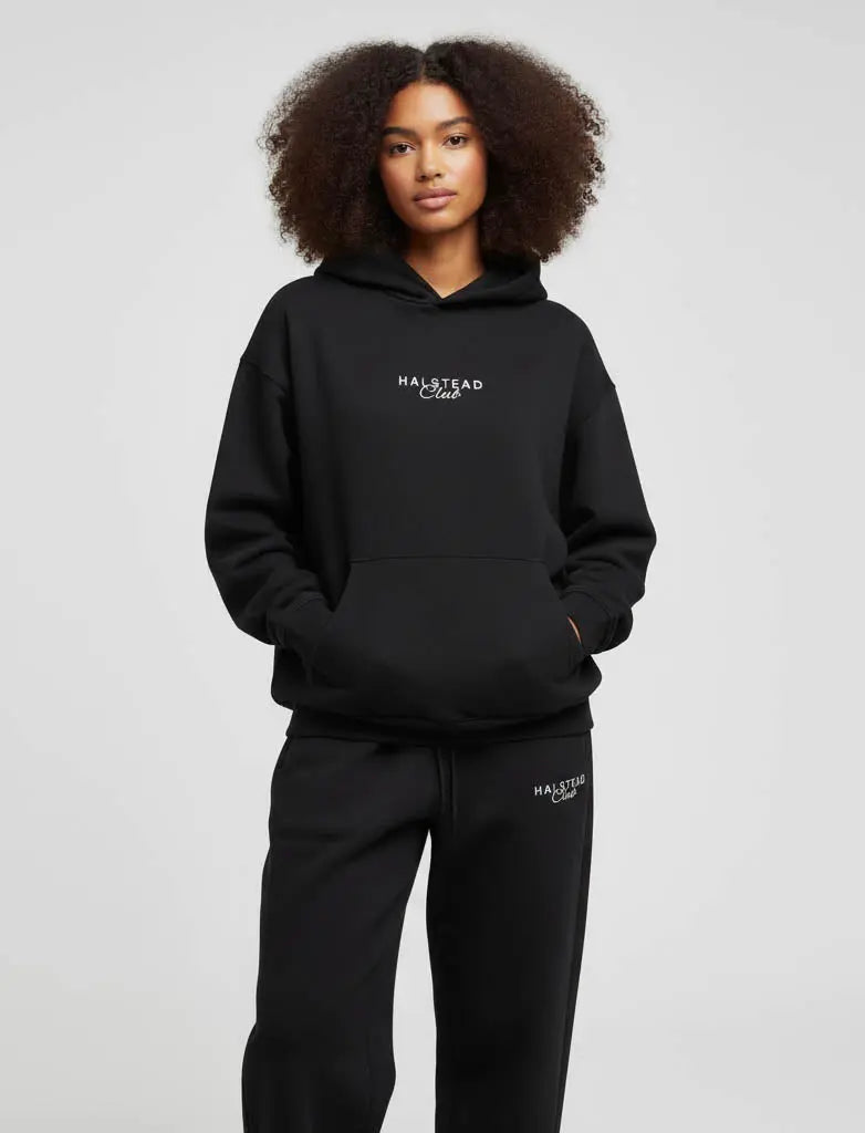 Person wearing a black hoodie and pants with 'Halstead' branding on a light gray background