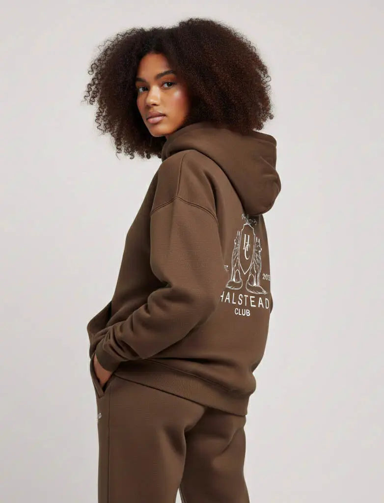 Person wearing a brown hoodie with a logo on the sleeve against a plain background