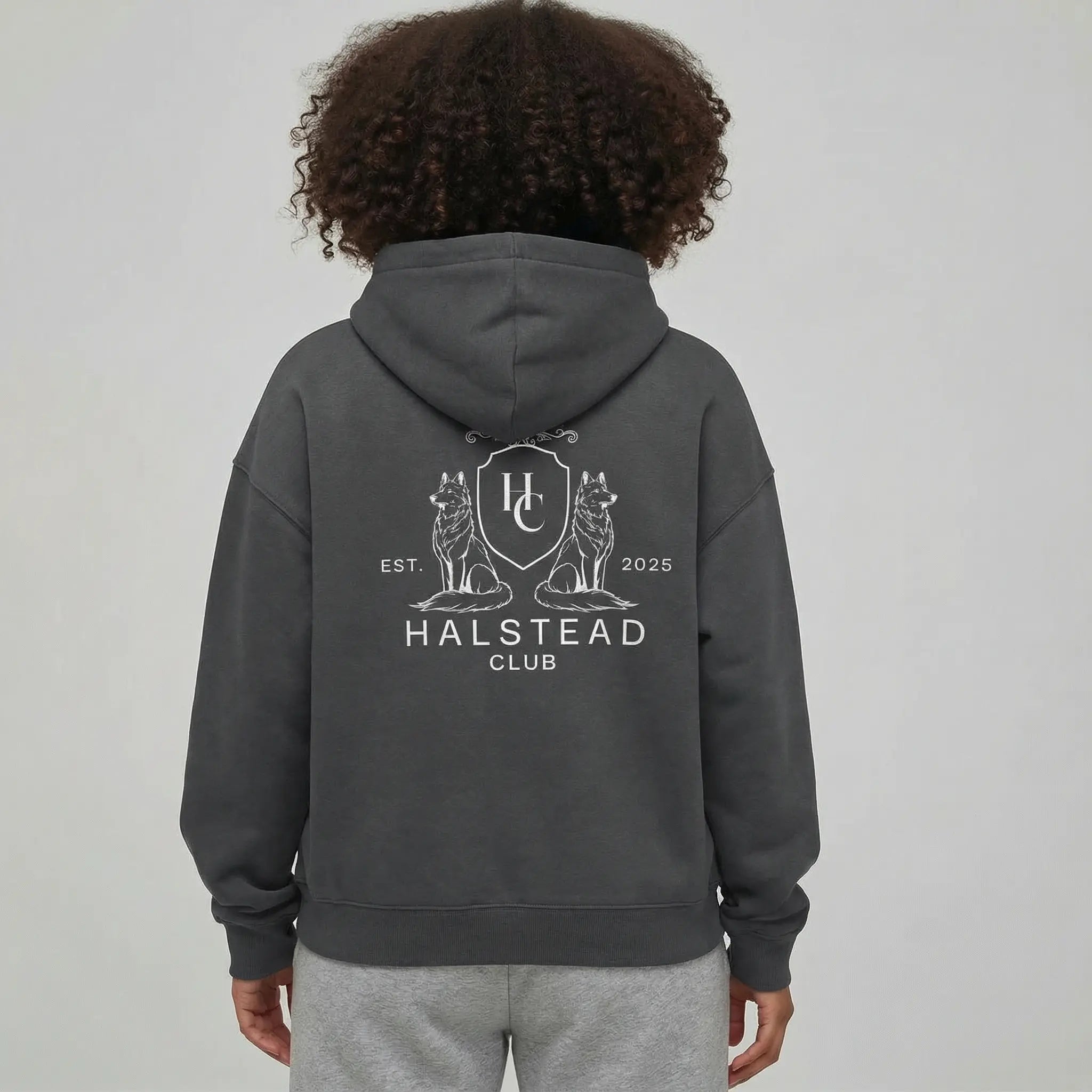 Person wearing a dark gray hoodie with 'Halstead Club' logo on the back against a light gray background