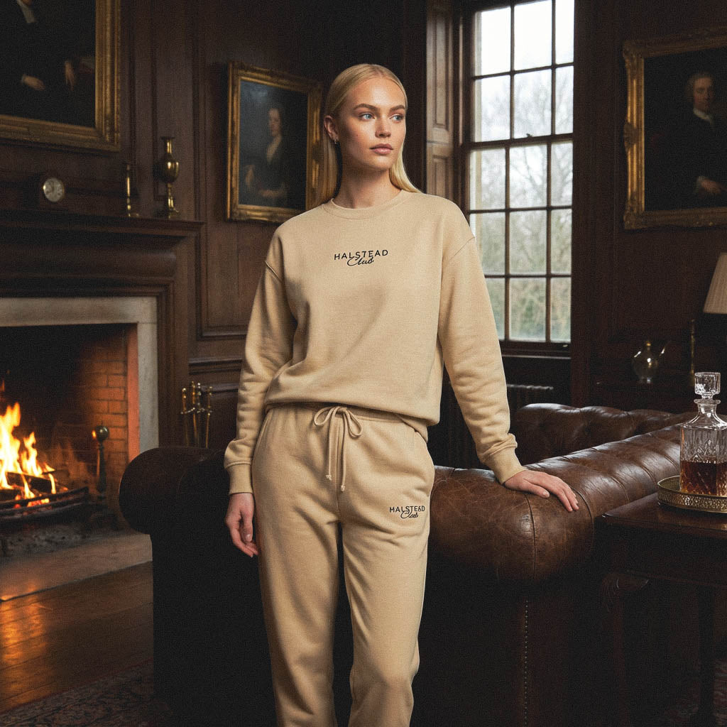 Woman in beige tracksuit standing in a room with a fireplace and paintings.