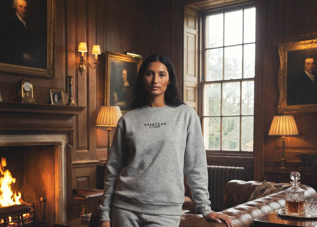 Woman wearing a gray sweatshirt with 'HALSTED' logo in an elegant room with fireplaces and paintings.