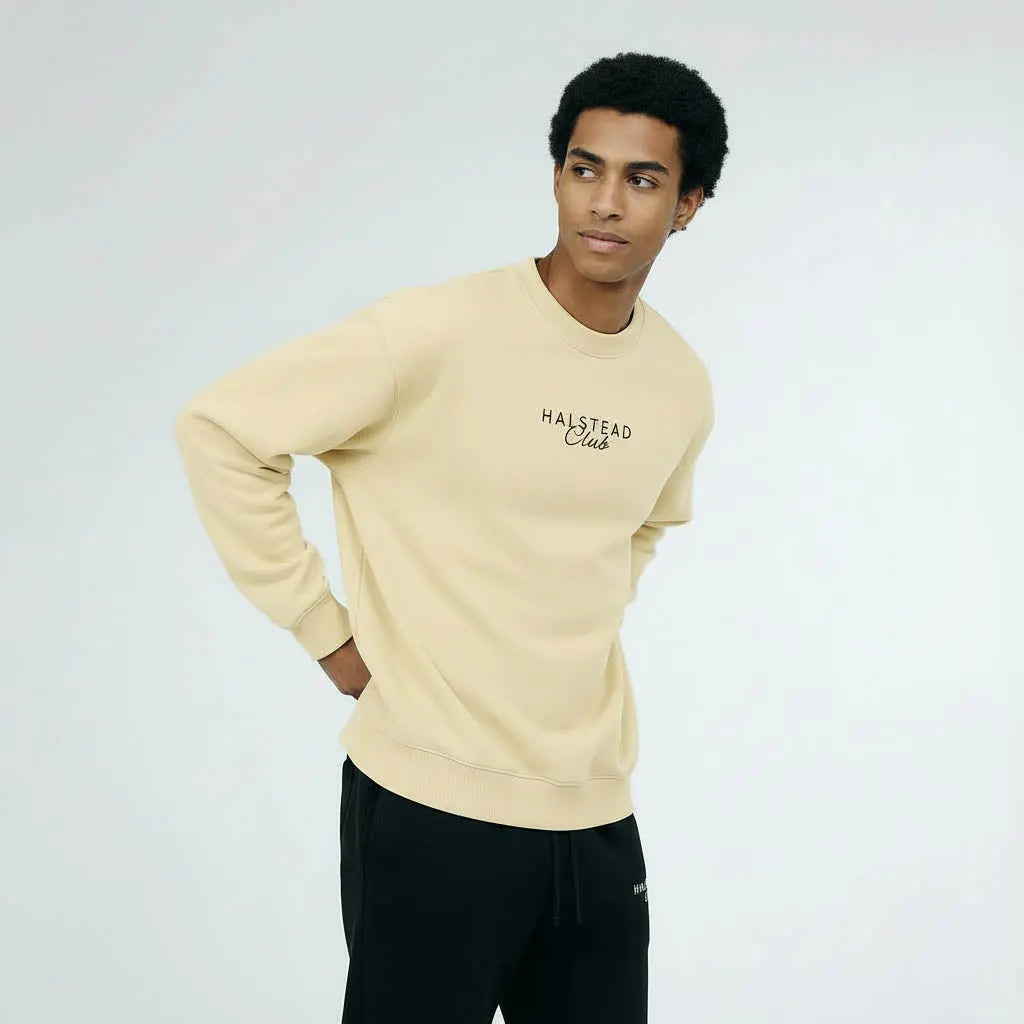 Man wearing a beige sweatshirt with 'Halstead Club' text on a plain background