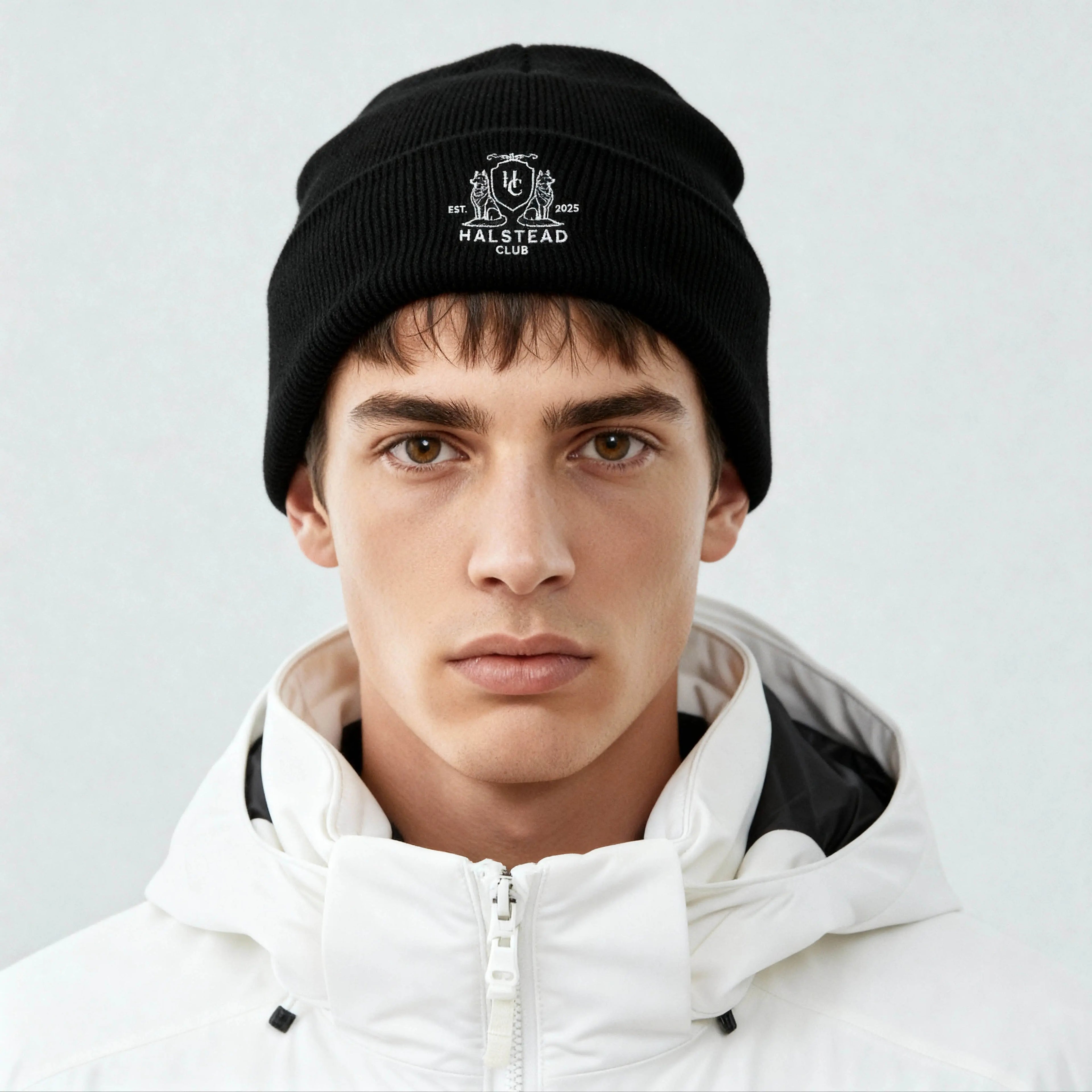Person wearing a black beanie with a logo and white jacket on a light gray background