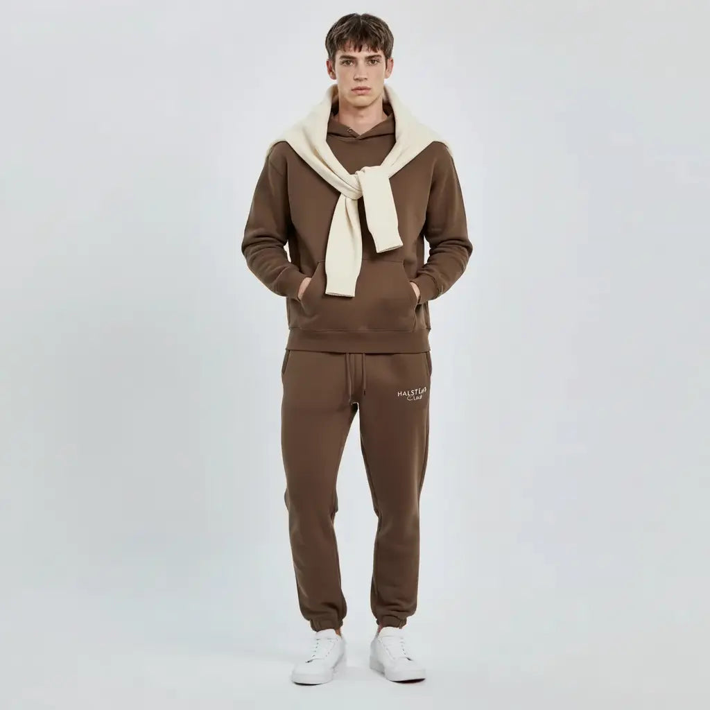 Man wearing a brown tracksuit with a white scarf on a light gray background