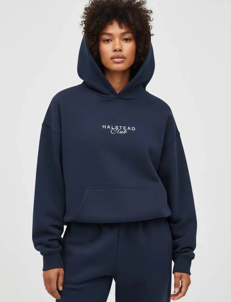 Person wearing a navy hoodie with 'Halstead Club' logo on a light gray background
