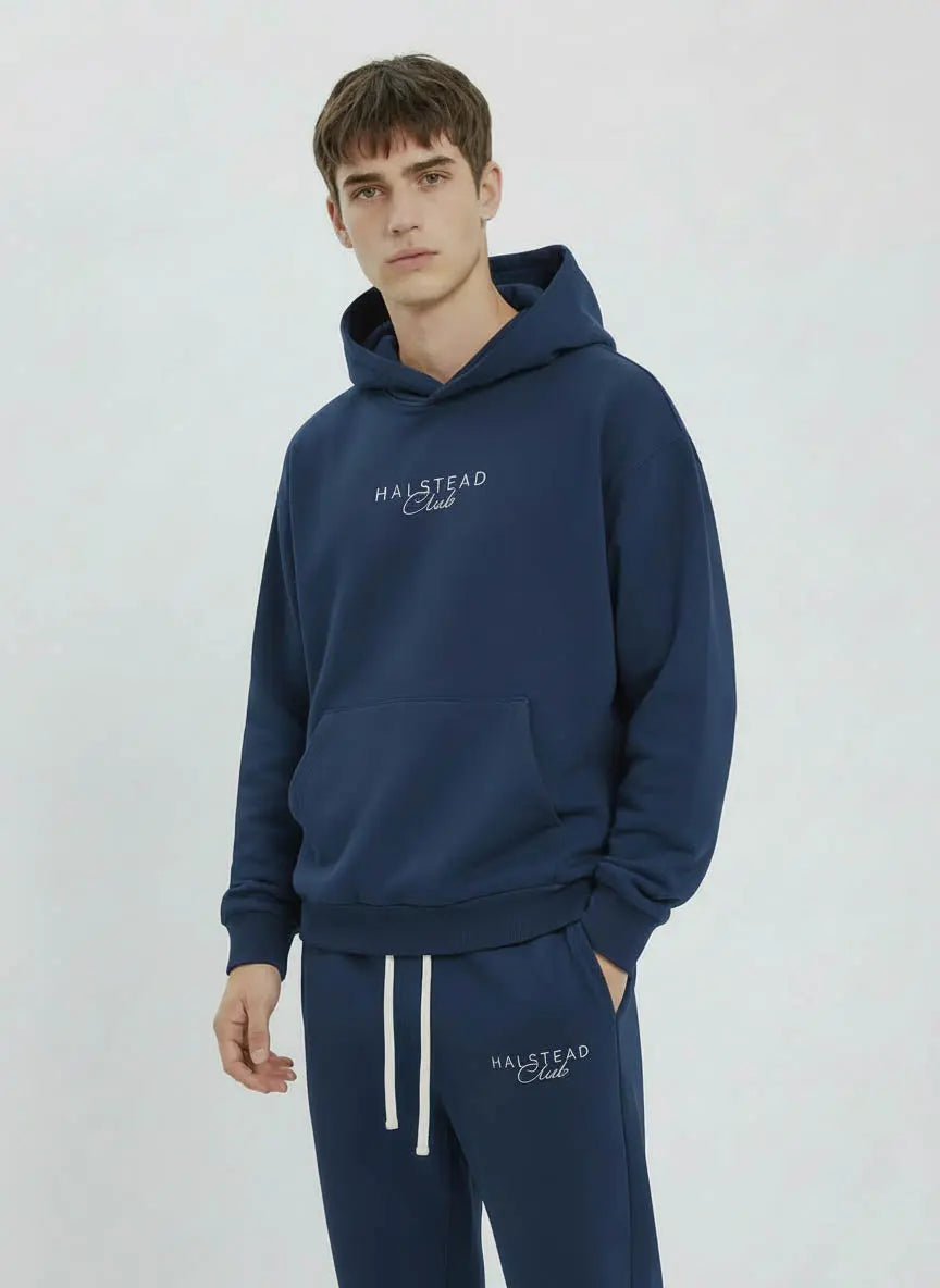 Man wearing a navy blue hoodie and pants with 'Halstead Club' branding on a light gray background