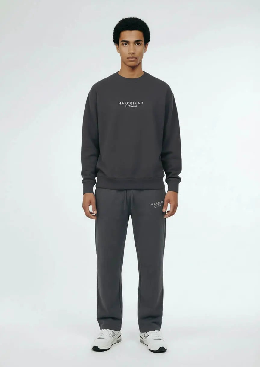 Person wearing a dark gray sweatshirt and pants with brand logos on a white background