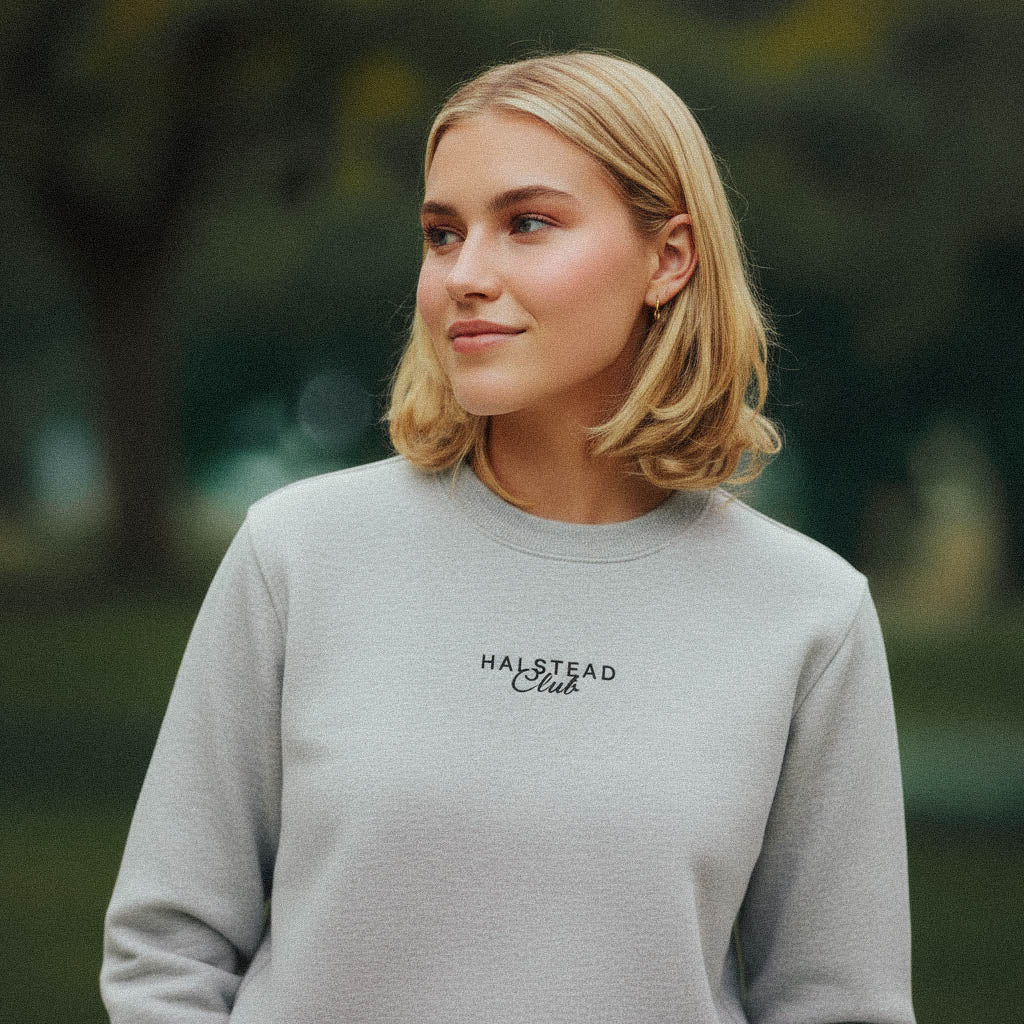 Woman wearing a gray sweatshirt with 'Halfstead Club' text outdoors