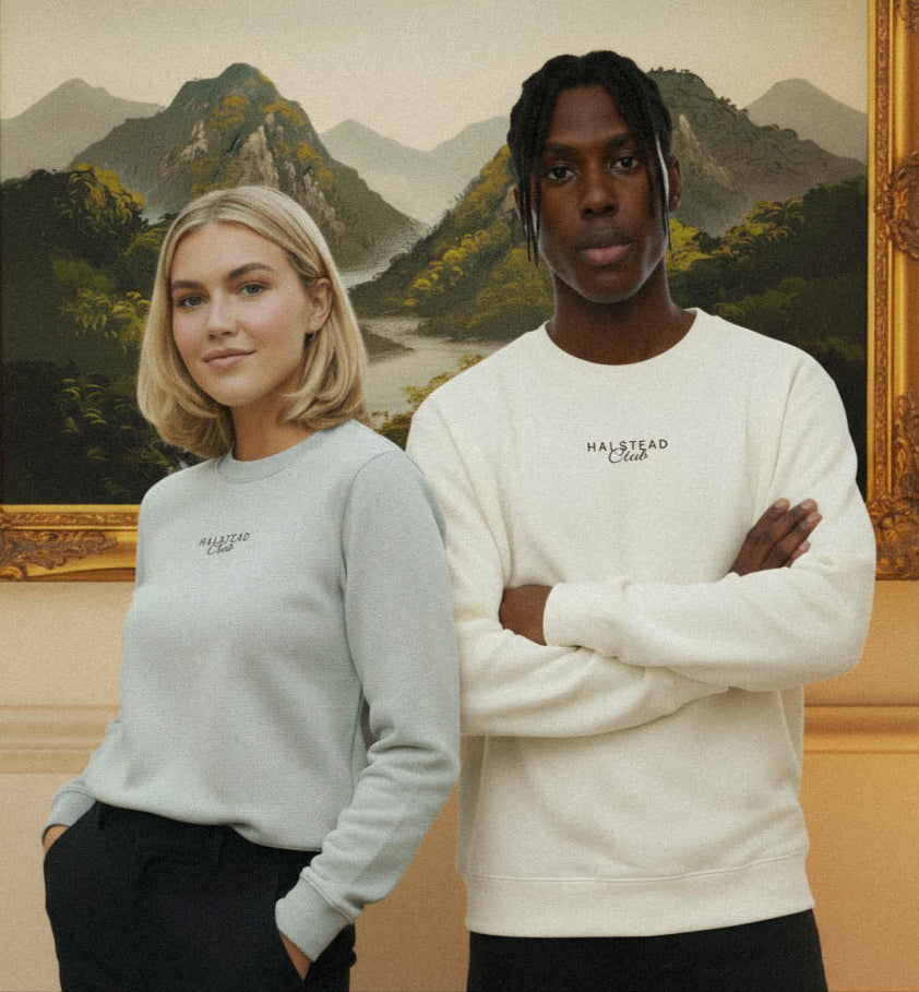 Two people wearing sweatshirts with a brand logo in front of a framed landscape painting.