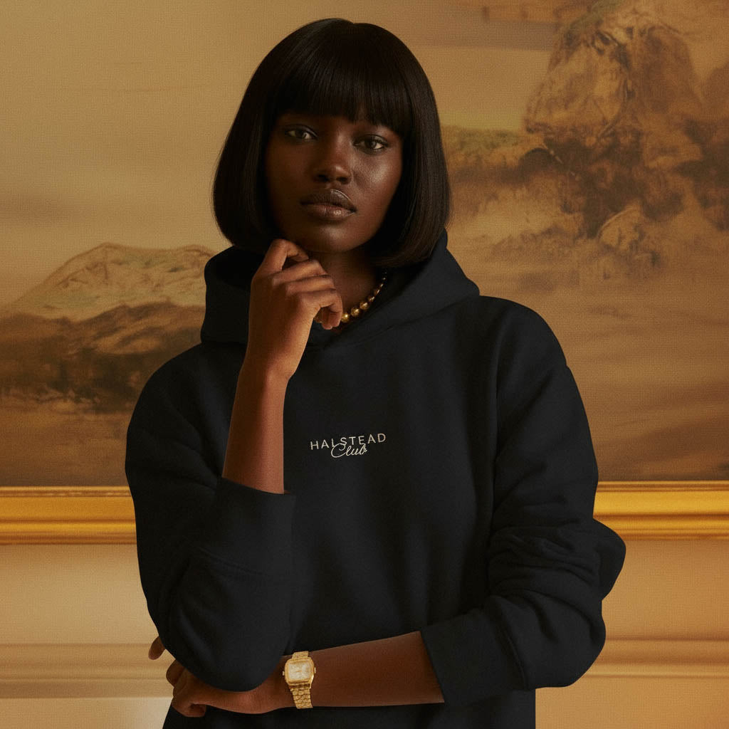 Person wearing a black hoodie with 'Halstead Club' text, standing against a warm-toned wall.