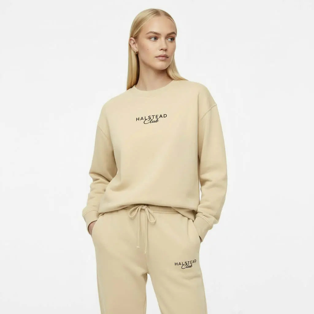 Woman wearing a beige 'Malstead Club' sweatshirt and pants on a white background