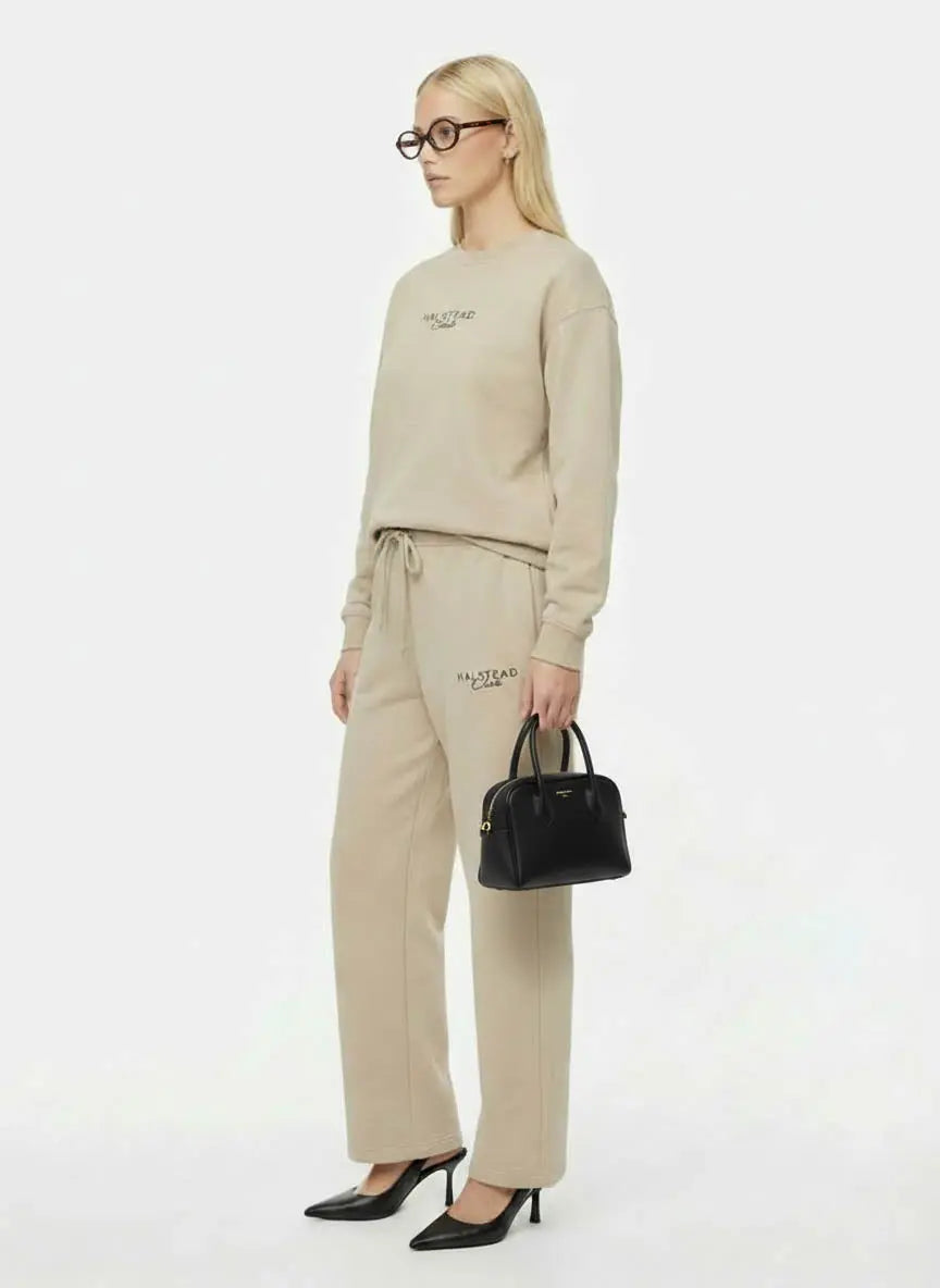 Woman wearing a beige tracksuit with 'Valentino' branding, holding a black handbag on a white background.